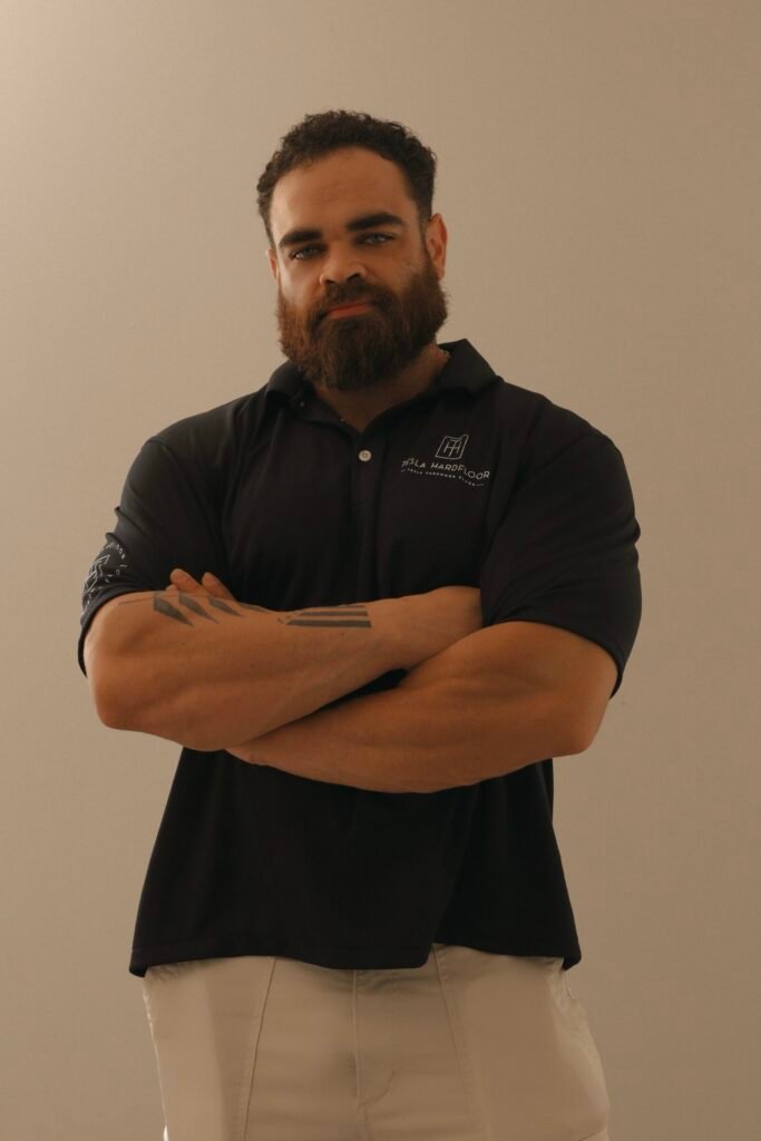 Owner of Tesla Hardfloor wearing company uniform, arms crossed, confident posture, beige background professional portrait for About Us section.