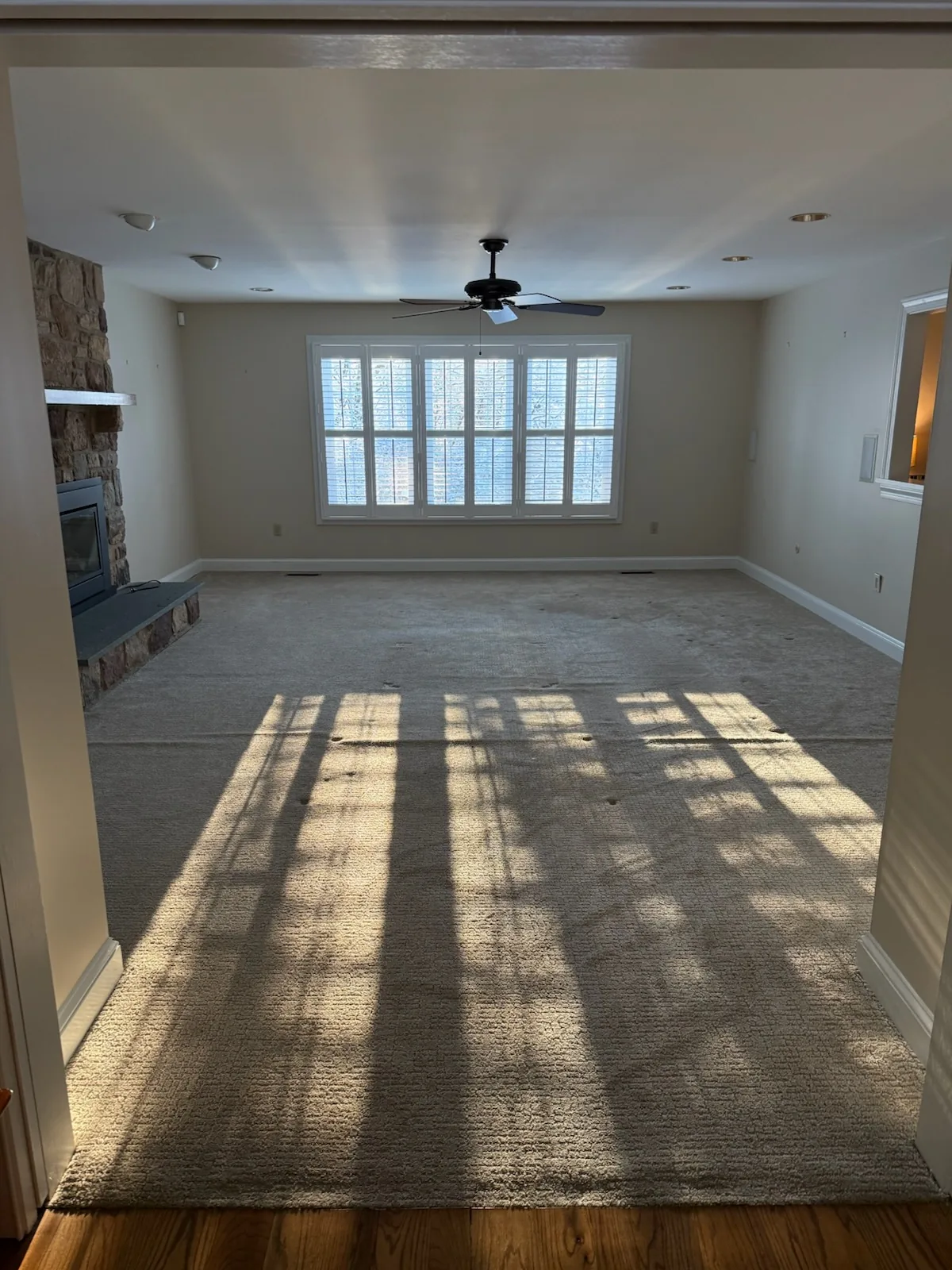 Empty living room with worn carpet and stone fireplace before hardwood floor installation in Doylestown, PA