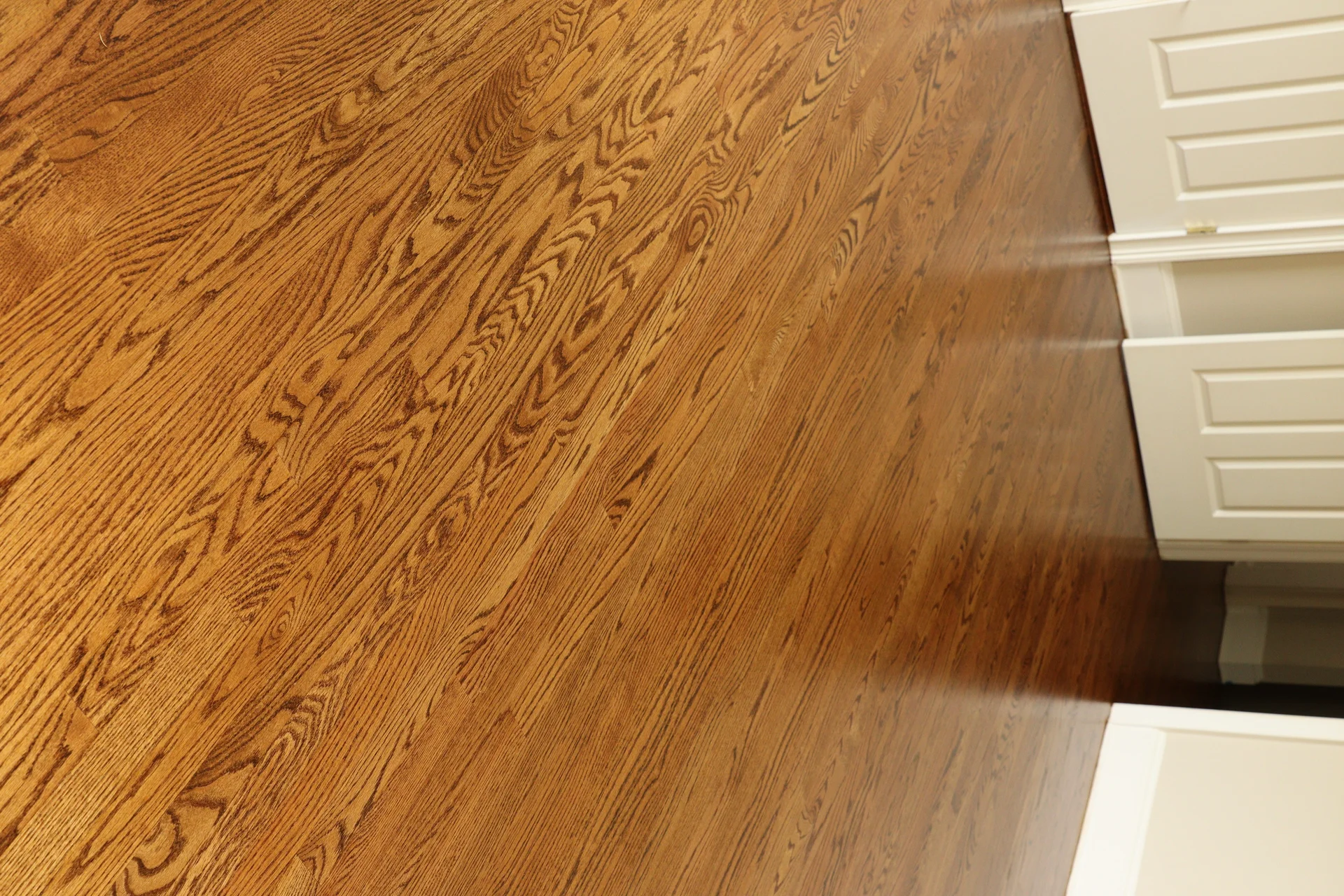 Beautifully refinished hardwood flooring with rich brown tones next to white cabinetry. by Tesla Hardfloor in West Chester, P