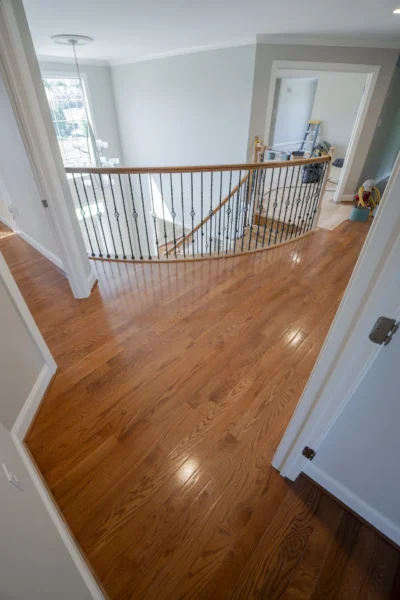 Beautifully refinished red oak hardwood floors with a glossy finish on a landing with stairs. by Tesla Hardfloor in Newtown,