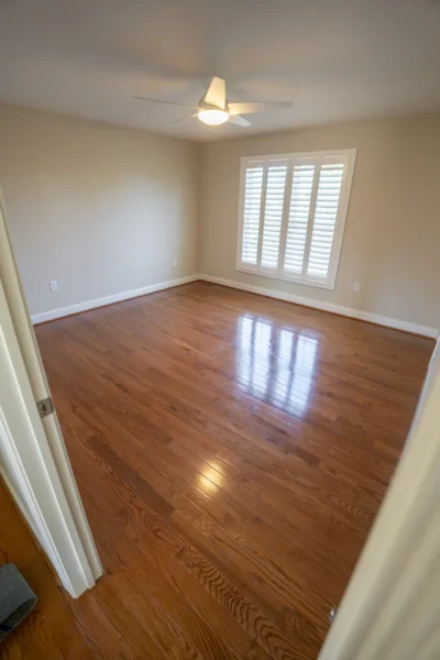 Empty room with newly refinished glossy hardwood floors, light beige walls, and white trim. by Tesla Hardfloor in Moorestown,