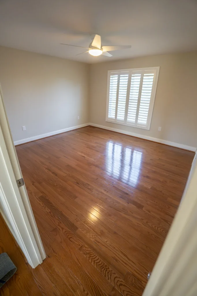Empty room with newly refinished glossy hardwood floors, light beige walls, and white trim. by Tesla Hardfloor in Moorestown,
