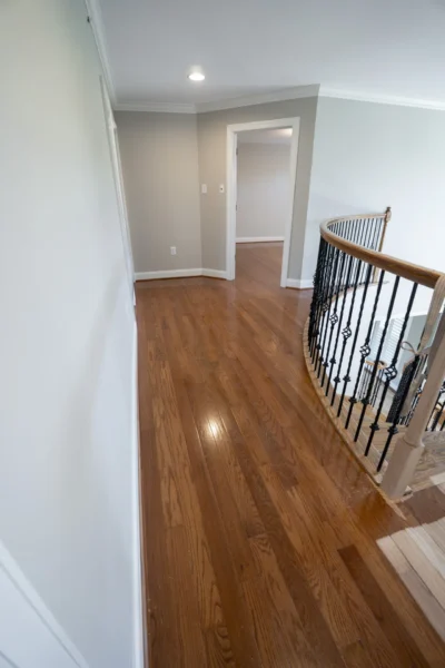 Hardwood floor refinishing in a hallway with a curved staircase and light gray walls. by Tesla Hardfloor in Doylestown, PA