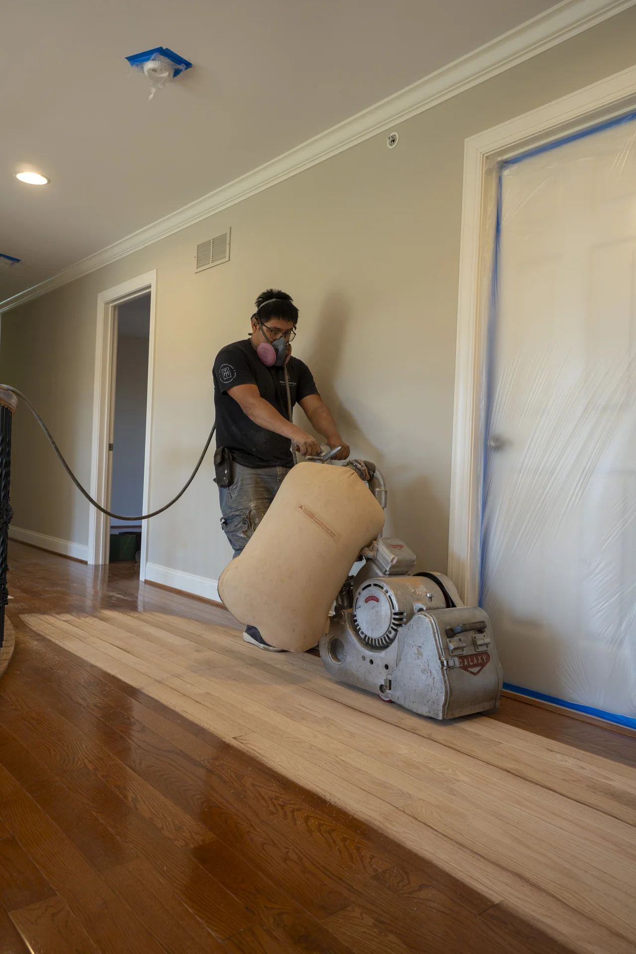 Hardwood Floor Sanding in West Chester, PA Worker sanding hardwood floors in a hallway, showing before and after refinishing. by Tesla Hardfloor in West Chester, PA