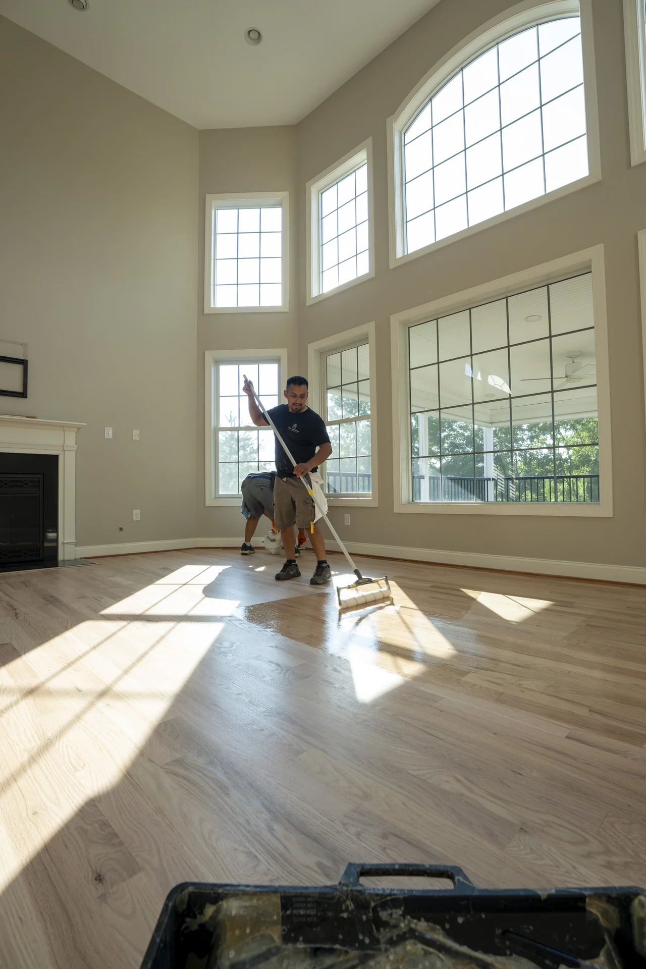 Applying Finish to Hardwood Floors in West Chester Workers applying finish to light natural hardwood floors in a bright living room. by Tesla Hardfloor in West Chester, PA