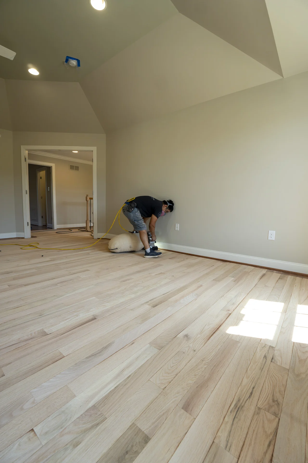 Worker installing light-colored hardwood flooring in a spacious room with light beige walls. by Tesla Hardfloor in Doylestown, PA