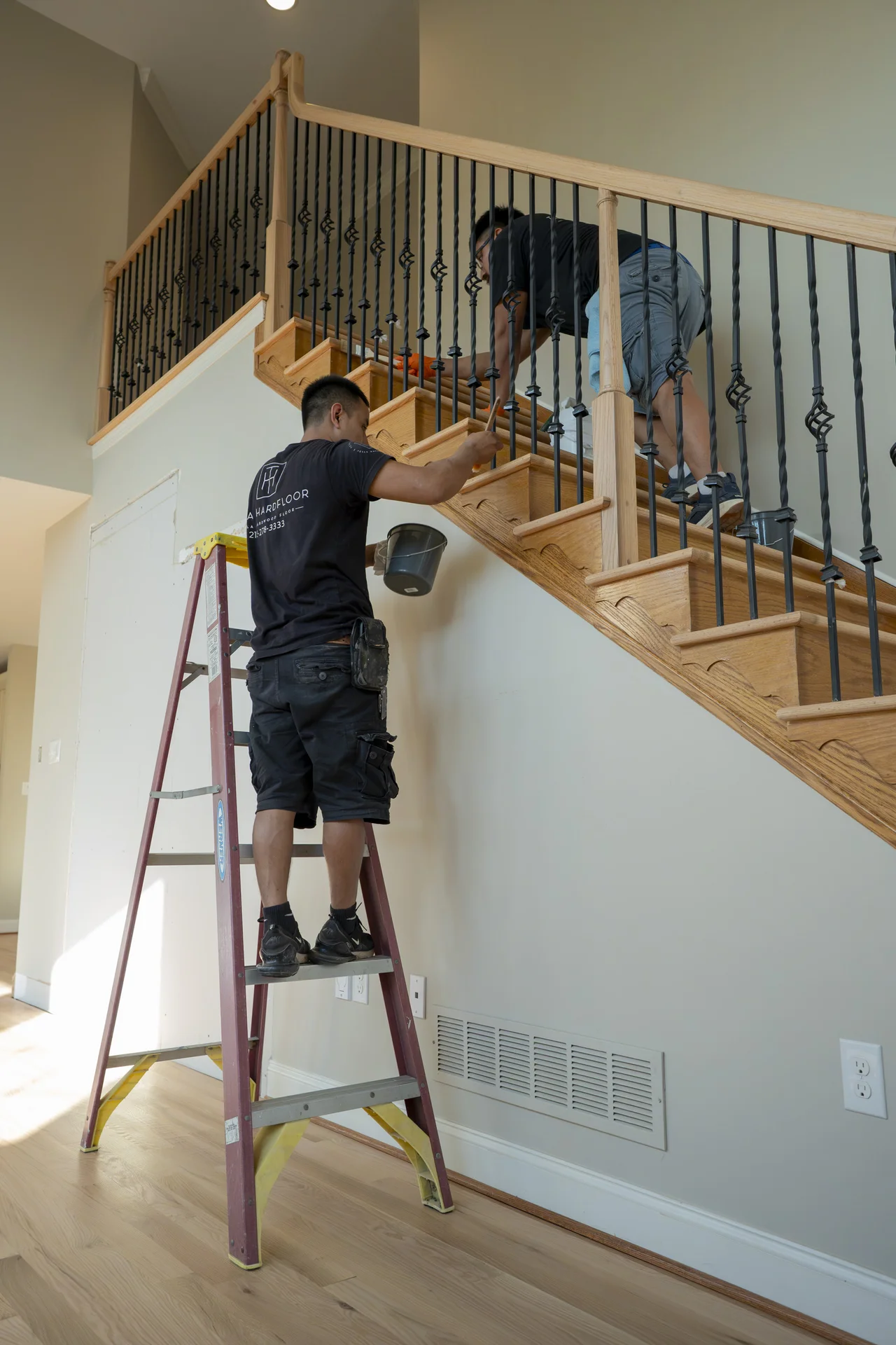 Stair Finishing by Tesla Hardfloor Professionals Workers applying finish to a light wood staircase with black wrought iron balusters and light walls. by Tesla Hardfloor in Vi