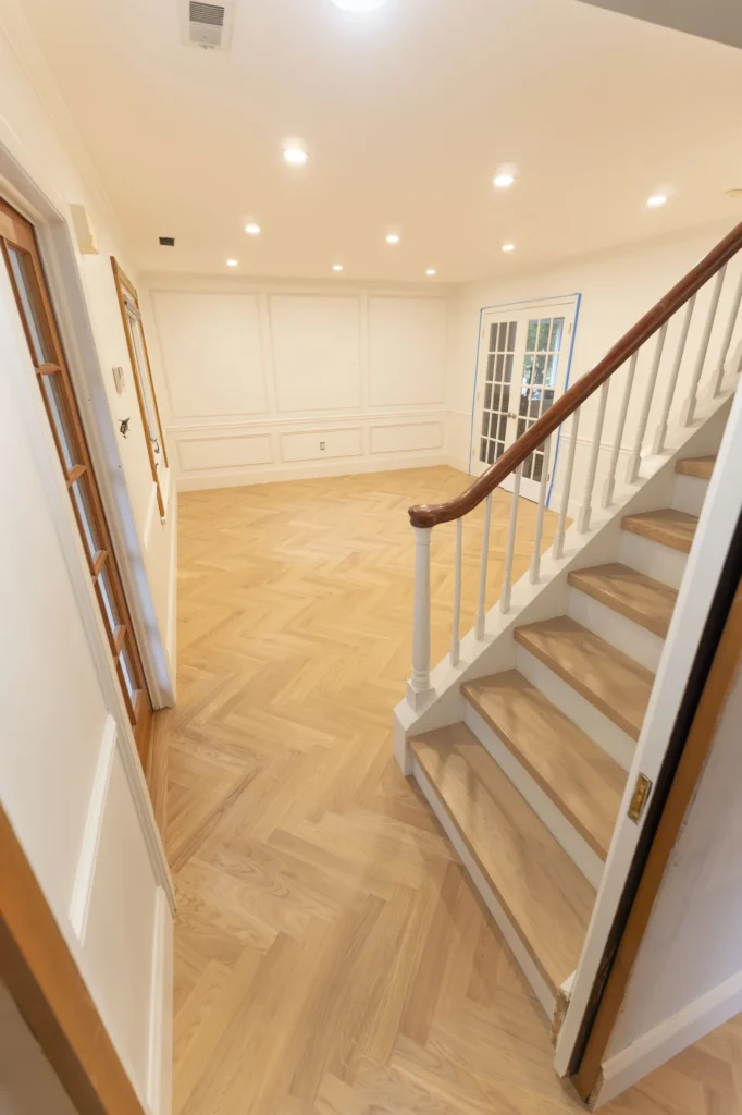 Light oak herringbone hardwood floor and oak stair treads in a room with white wall molding and French doors