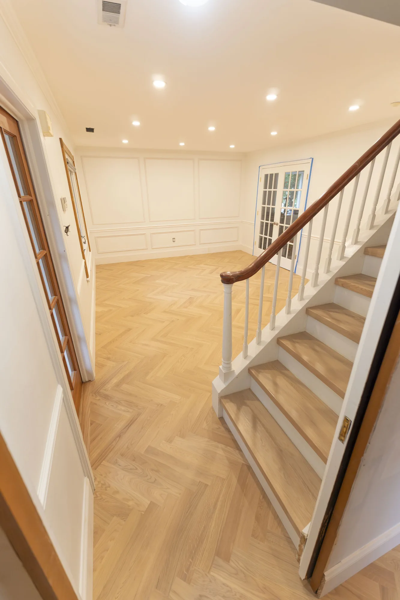 Herringbone hardwood floor and matching stair treads in a paneled room with French doors in Lafayette Hill, PA