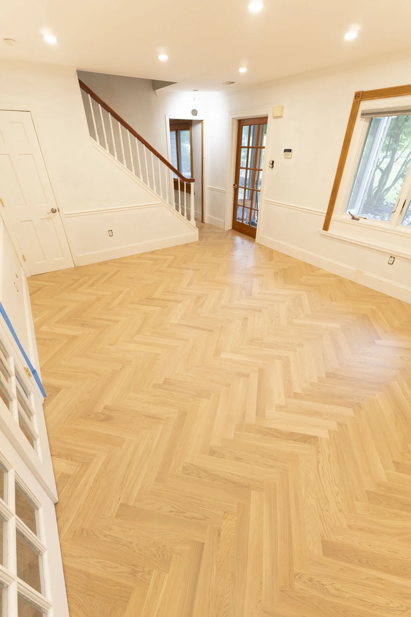 Light herringbone hardwood floor in a bright Lafayette Hill, PA living area with a white staircase, installed by Tesla Hardfloor