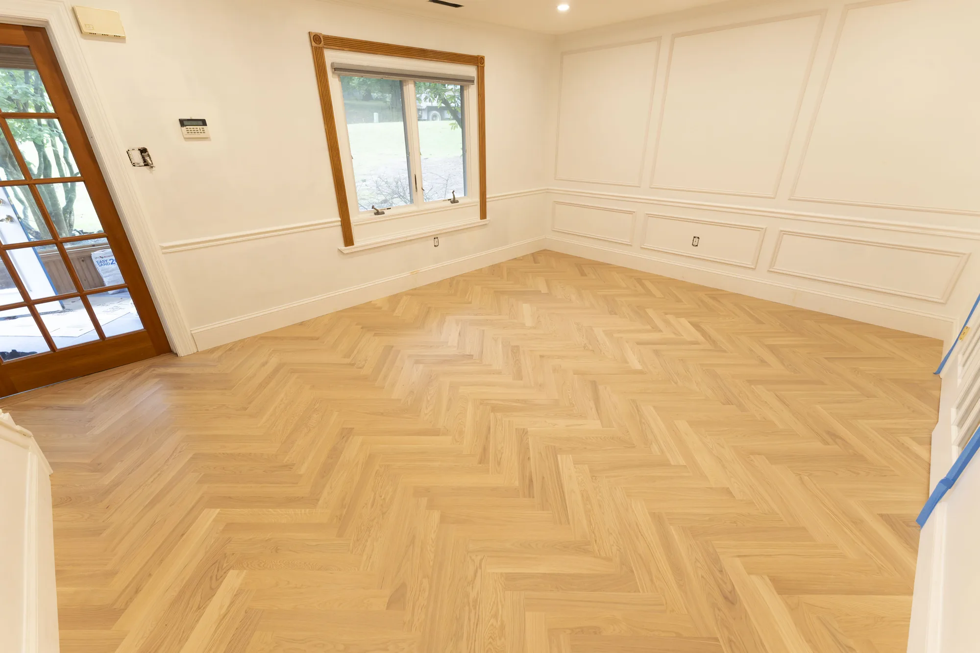 Wide view of a light herringbone hardwood floor across a bright room with white wall paneling in Lafayette Hill, PA