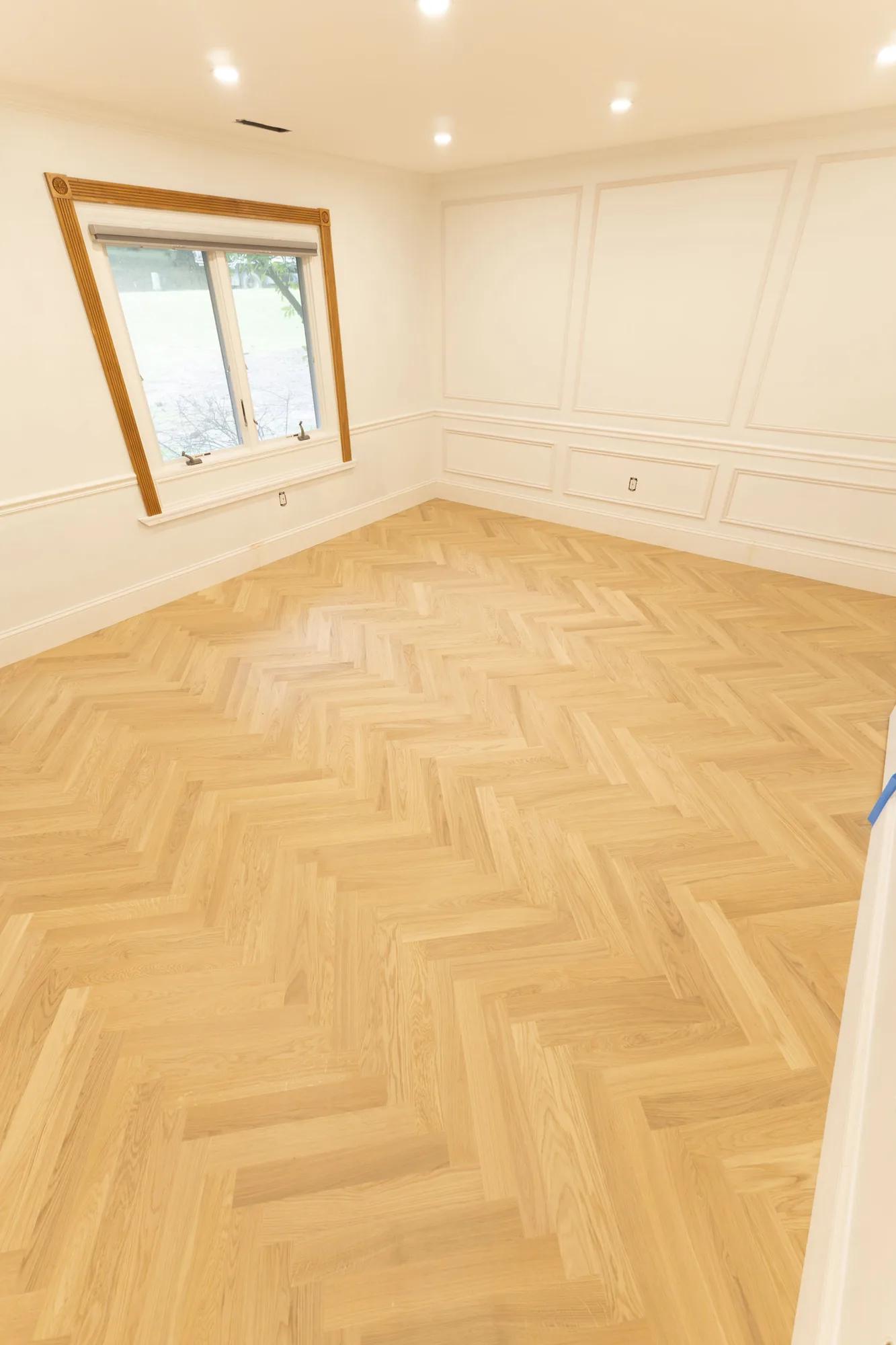 Herringbone hardwood floor in a Lafayette Hill, PA room with white wainscoting and a wood-trimmed window